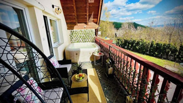 A balcony with a wooden ceiling, a small table with fruit, a chair, and a view of a green landscape. - Cavljak Retreat Sarajevo - Mountain Home - Jakuzzi (Sarajevo)