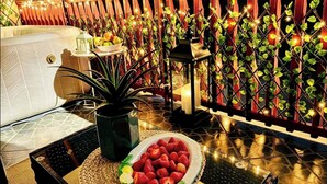 A terrace with a table, potted plants, a bowl of fruit, and a decorative wall with climbing plants and string lights. - Cavljak Retreat Sarajevo - Mountain Home - Jakuzzi (Sarajevo)