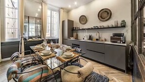 Une cuisine moderne avec un coin repas, comprenant une table en verre, des chaises à rayures et un comptoir de cuisine agrémenté d’appareils électroménagers et d’objets décoratifs.