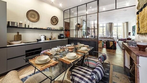 Une cuisine moderne avec un coin repas, comprenant un grand îlot central, des appareils électroménagers contemporains et une vue sur le salon.