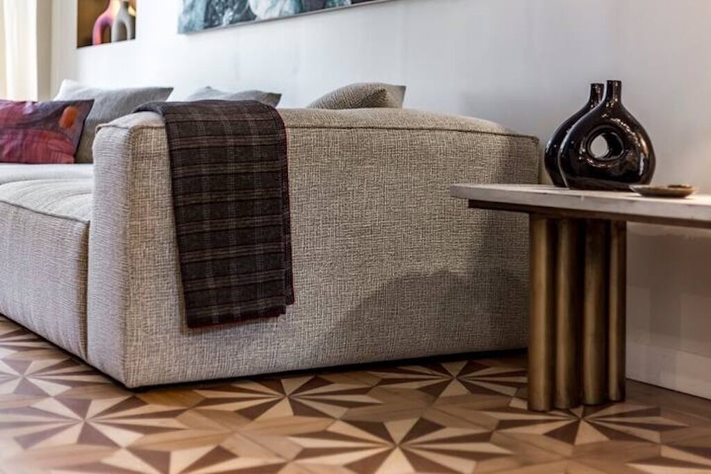 A sofa with a plaid throw blanket, a vase, and a geometric patterned floor.