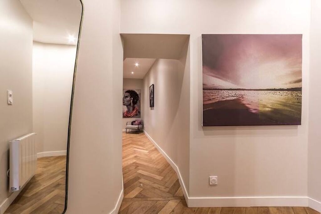Un couloir avec un parquet en point de Hongrie, un radiateur et un tableau accroché au mur.