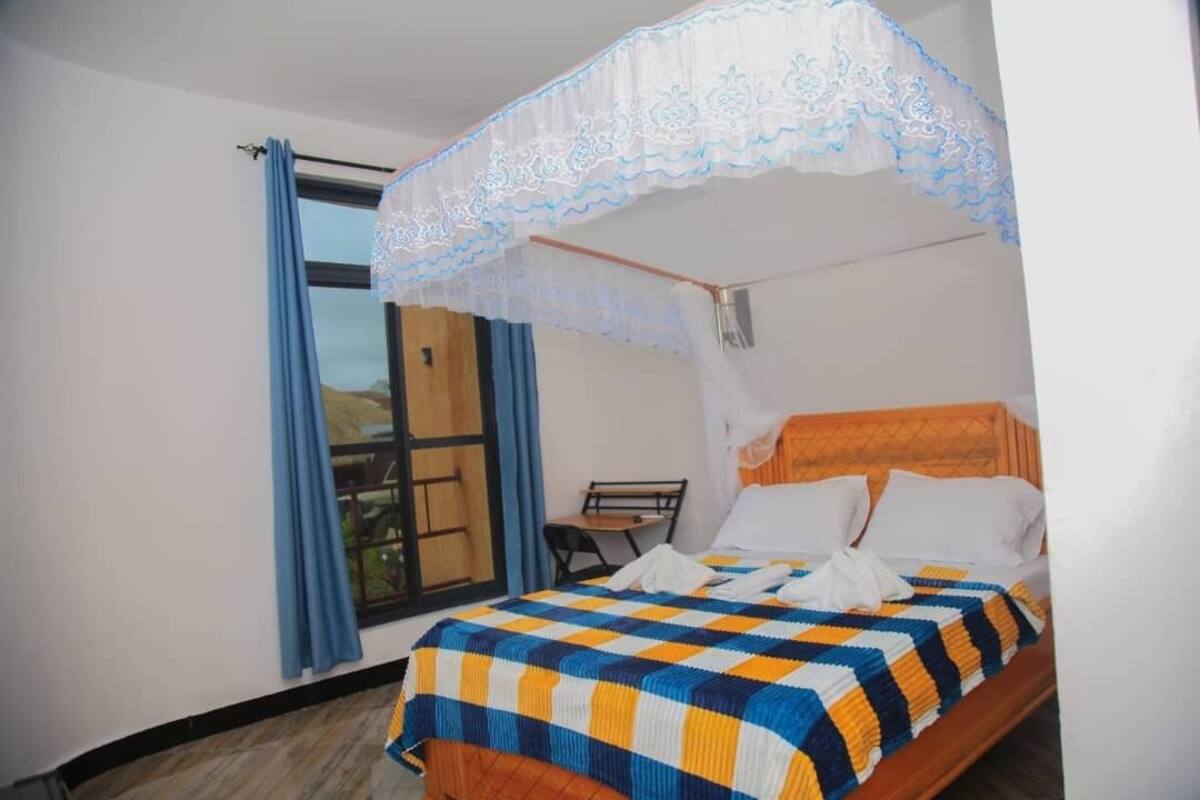 Una cama individual con colcha a cuadros, cabecera de madera y dosel con detalles de encaje.