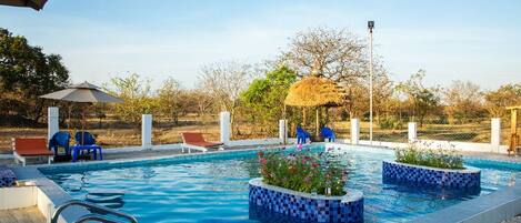 A swimming pool with a tiled border, lounge chairs, and a thatched structure.