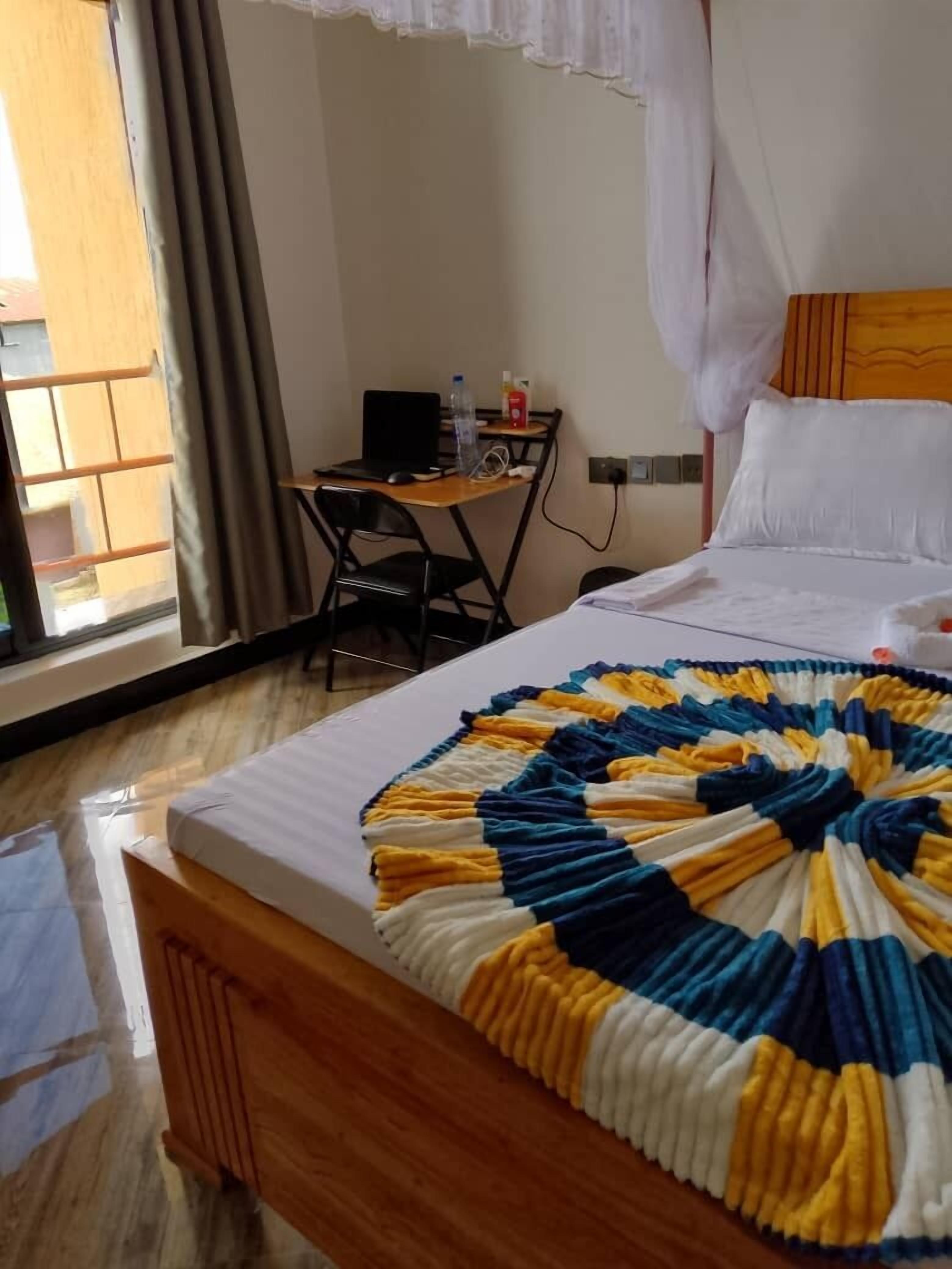 Una camera d'albergo con un letto, una scrivania, una sedia e una finestra con tende.