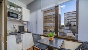 A compact kitchen with a microwave, toaster, and sink, a small dining table with chairs, and a view of a building through a window. - Studio 'Zizas House' with Wi-Fi and Air Conditioning (Portimão)
