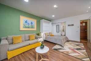 Een moderne woonkamer met een bank, een kleine tafel met een vaas, een bed en een 'WELCOME' bord.