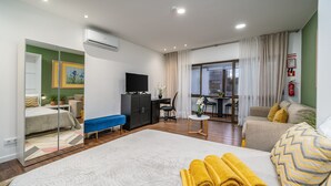 A hotel room with a bed, a desk, a sofa, a mirror, and a view of the outside. - Studio 'Zizas House' with Wi-Fi and Air Conditioning (Portimão)