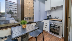 A compact kitchen with a dining area, a small table with a plant, and a view of a building outside. - Studio 'Zizas House' with Wi-Fi and Air Conditioning (Portimão)