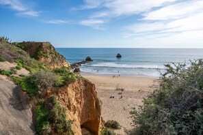 Uma praia costeira com falésias, um afloramento rochoso e uma faixa de areia.
