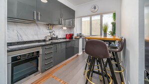 Een moderne keuken met donkere kastjes, een inbouwoven en een houten eettafel met barstoelen.