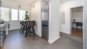 Een moderne keuken met een roestvrijstalen koelkast, een eethoek met krukken, en een zichtbare klok aan de muur.