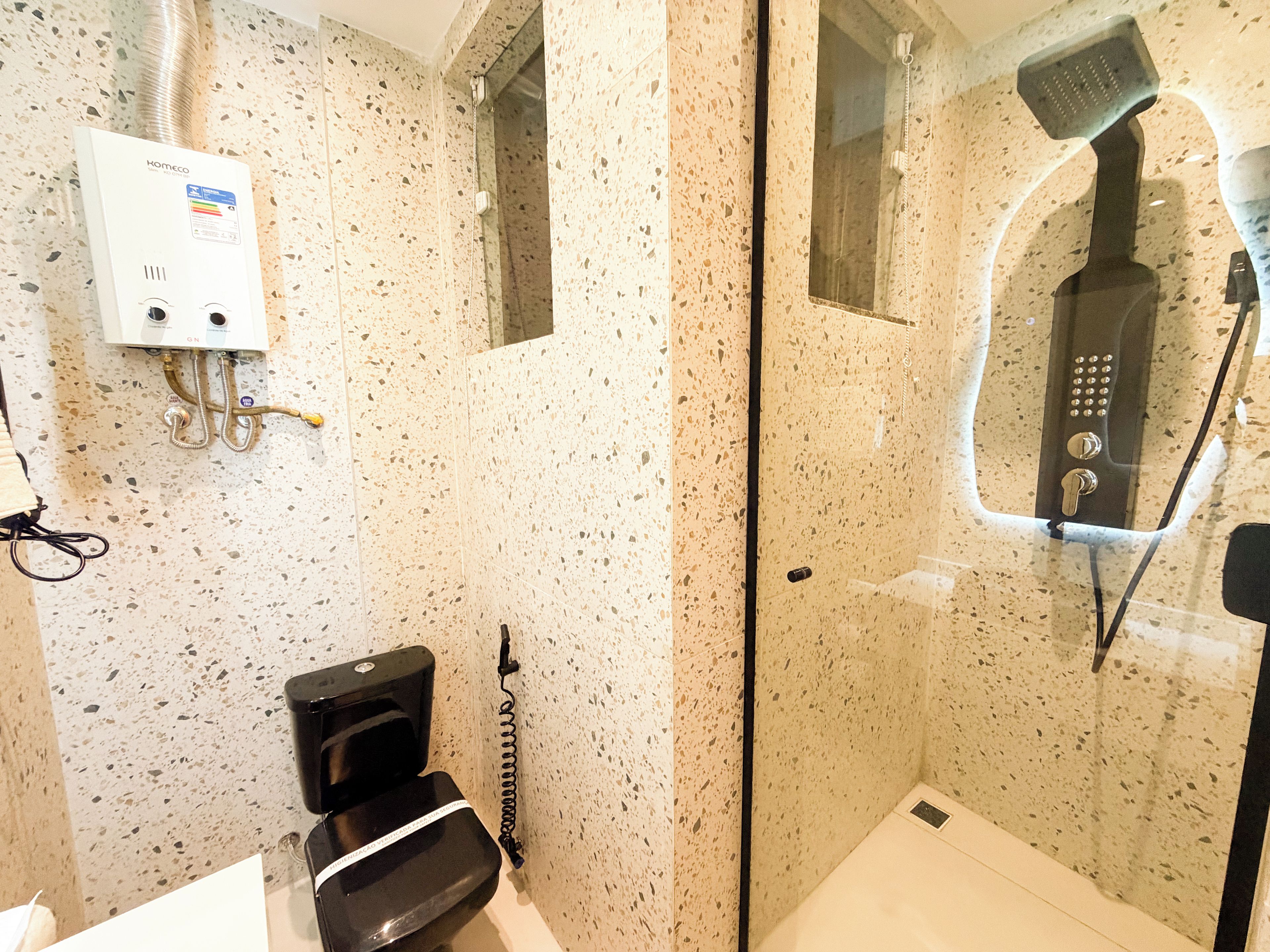 Ein Badezimmer mit Duschkabine, Toilette und Warmwasserbereiter.