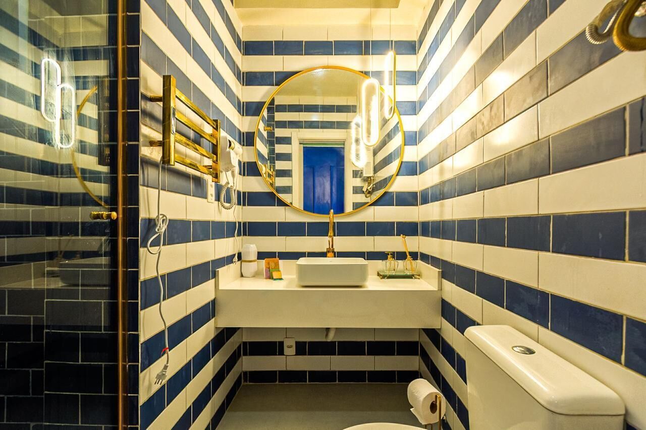 Un baño con baldosas azules y blancas a rayas, un espejo redondo, un lavabo blanco y un inodoro.