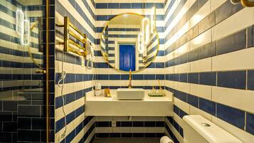 Un baño con baldosas azules y blancas a rayas, un espejo redondo, un lavabo blanco y un inodoro.