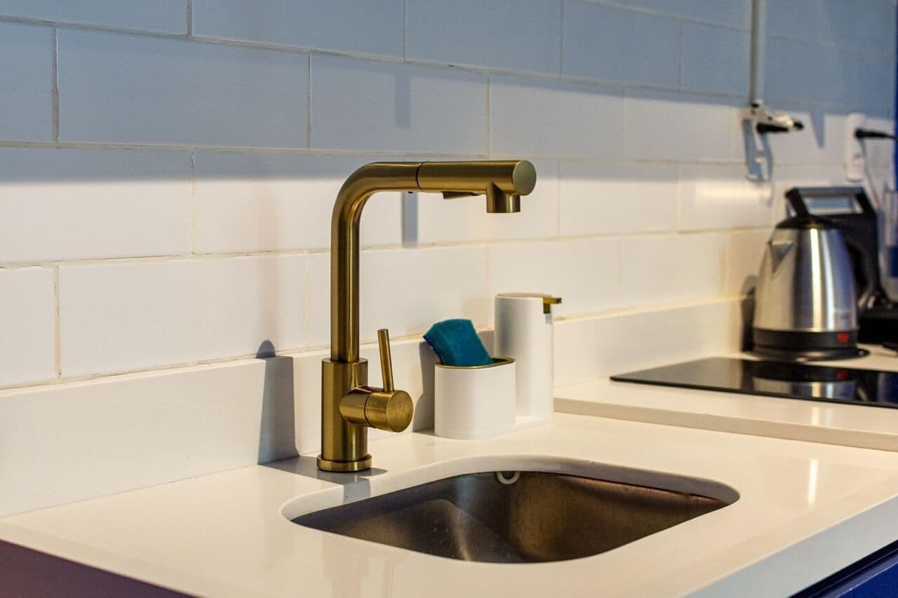 Een moderne keuken met een roestvrijstalen spoelbak, een gouden kraan en een waterkoker op het aanrecht.