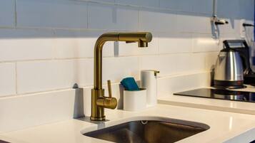 Een moderne keuken met een roestvrijstalen spoelbak, een gouden kraan en een waterkoker op het aanrecht.