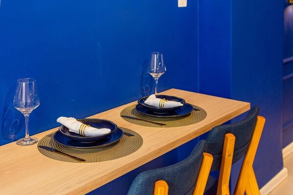 A dining table with two sets of plates, cutlery, and wine glasses, set against a blue wall. - StayHome Beira-Mar Copacabana Posto 6 (Rio de Janeiro)