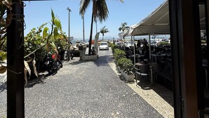 A cobblestone pathway leading to a covered outdoor seating area with umbrellas, surrounded by palm trees and parked cars. - StayHome Beira-Mar Copacabana Posto 6 (Rio de Janeiro)