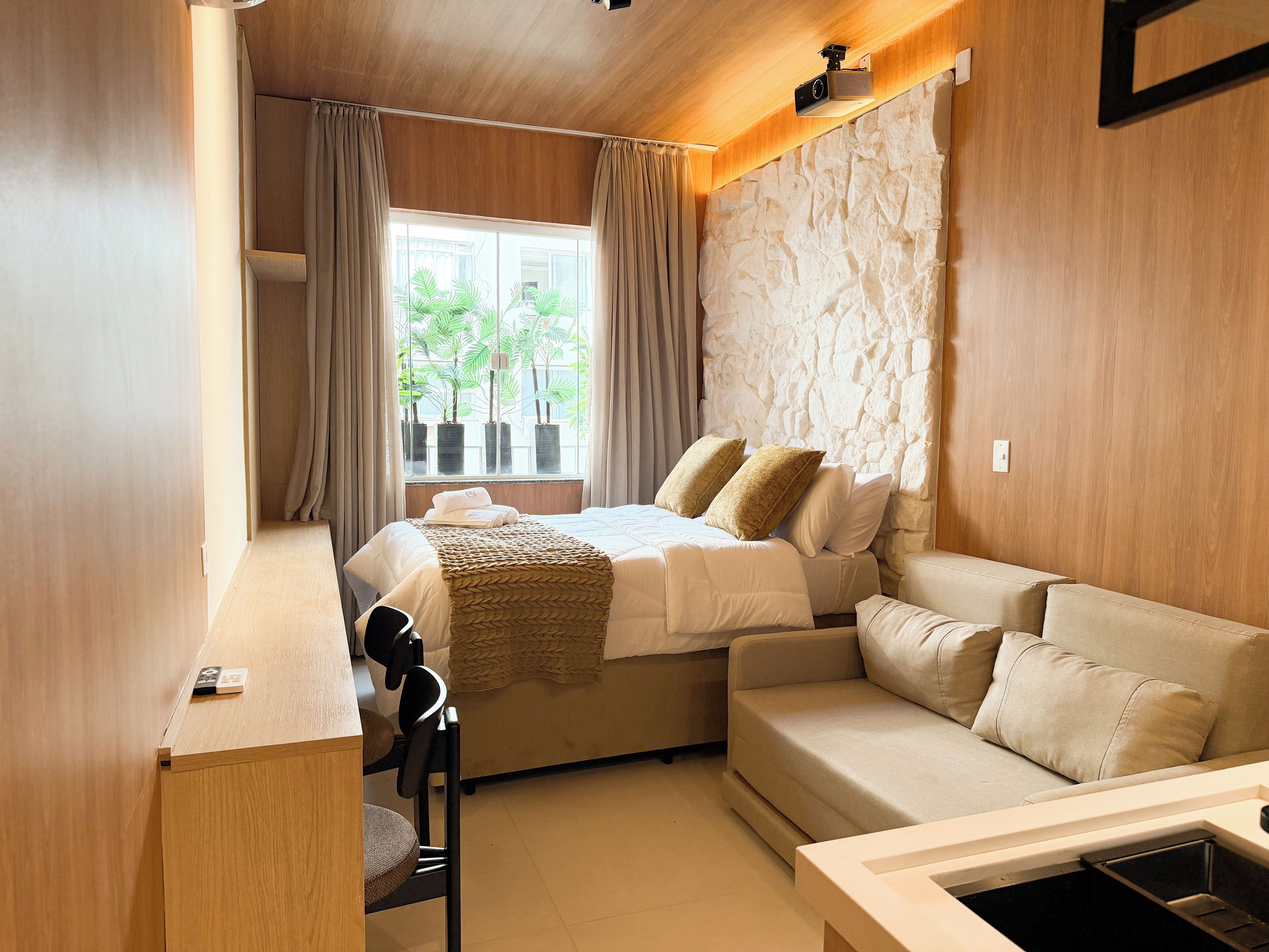 A hotel room with a bed, a sofa, a desk, and a window with curtains.