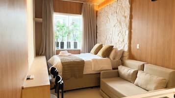 A hotel room with a bed, a sofa, a desk, and a window with curtains.