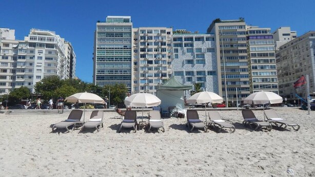 A beach with sun loungers and umbrellas, and high-rise buildings in the background. - StayHome Beira-Mar Copacabana Posto 6 (Rio de Janeiro)