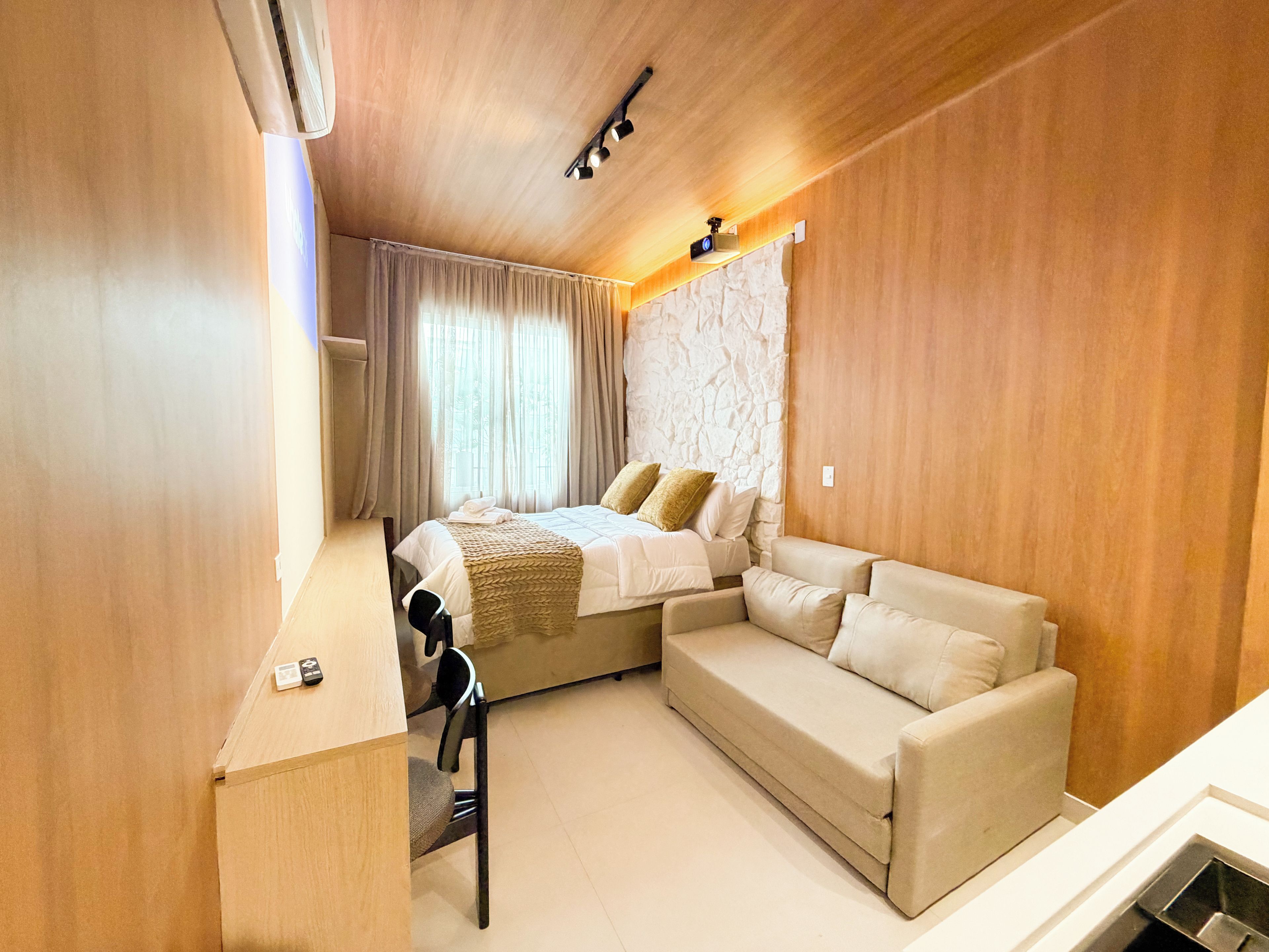 A compact hotel room with a bed, a sofa, a desk, and a chair.