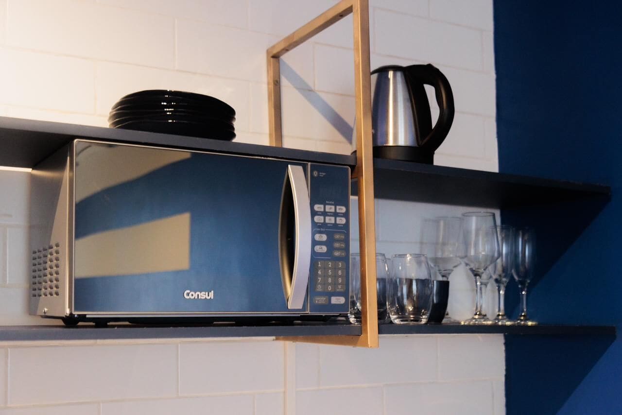 Eine Mikrowelle mit digitaler Anzeige und Bedienfeld, auf einer Ablage über einer gefliesten Wand platziert.