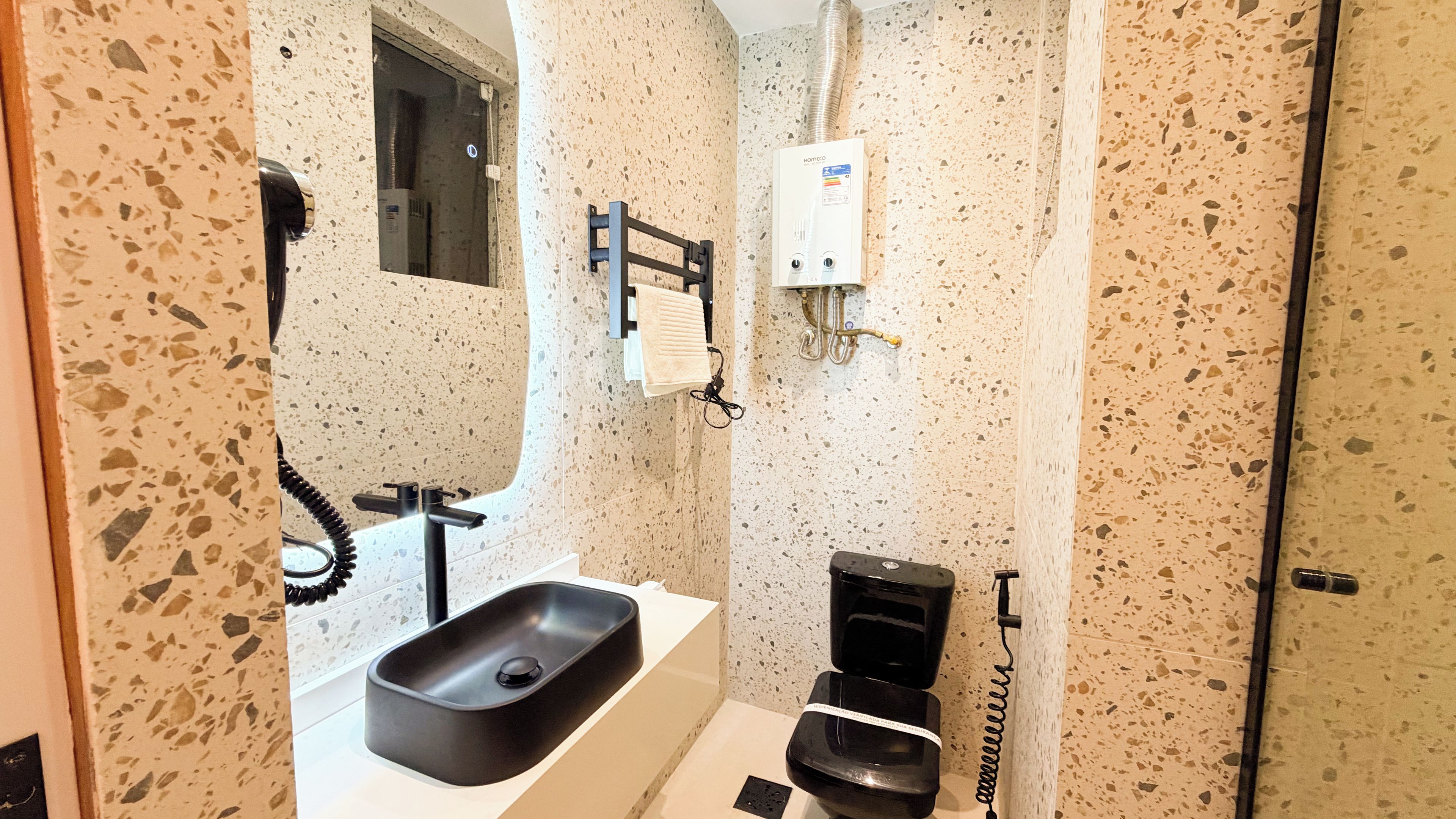 A bathroom with a white sink, a black toilet, a towel rack, and a water heater.