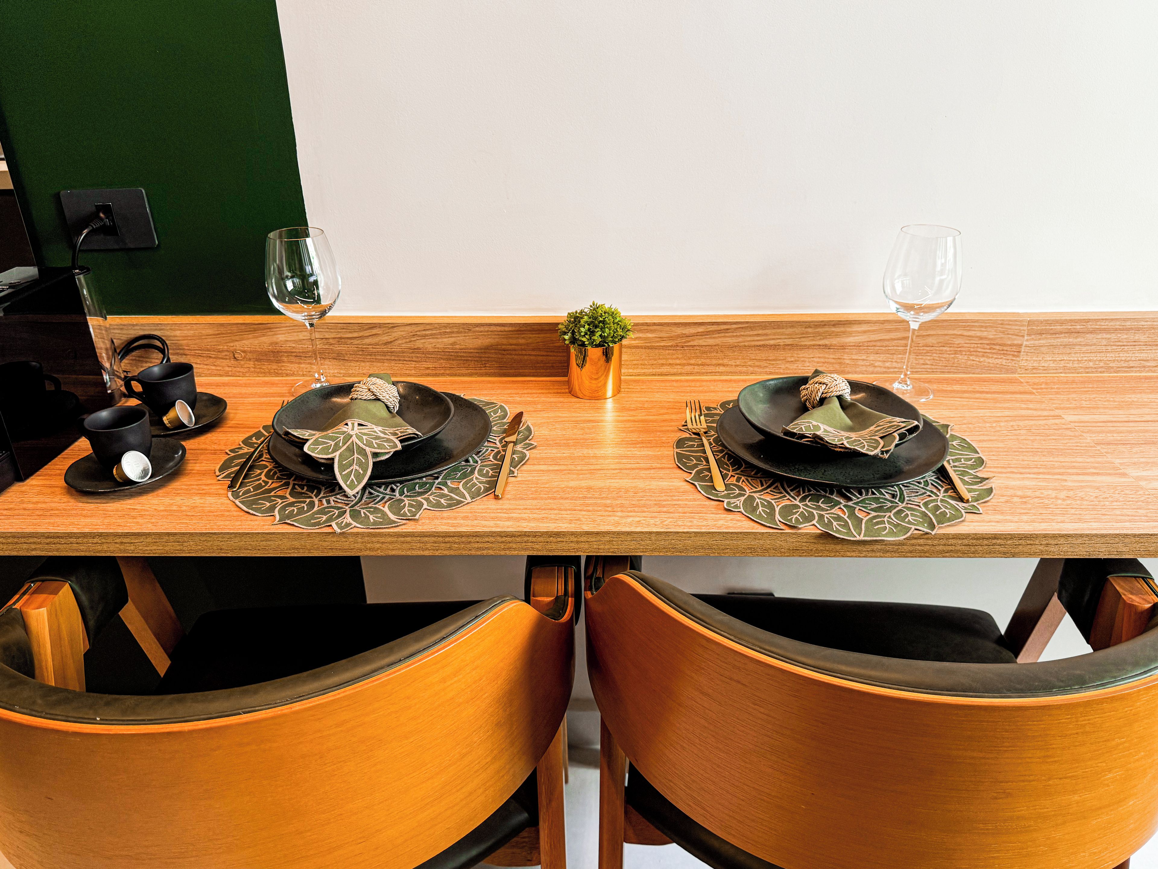 Una mesa de comedor dispuesta con platos, cubiertos y vasos, con dos sillas a cada lado.