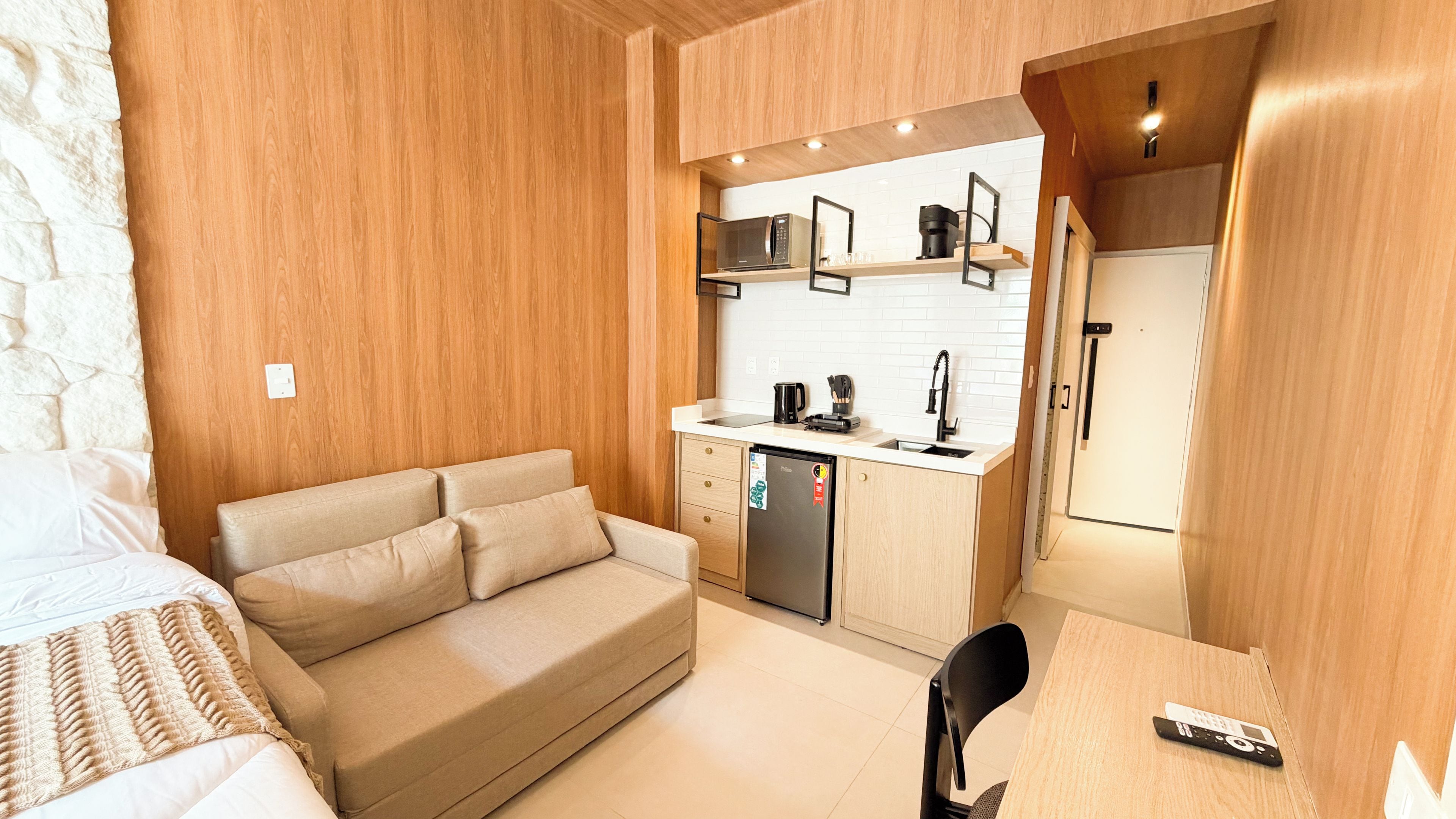 A compact room with a bed, a sofa, a kitchenette, and a desk.