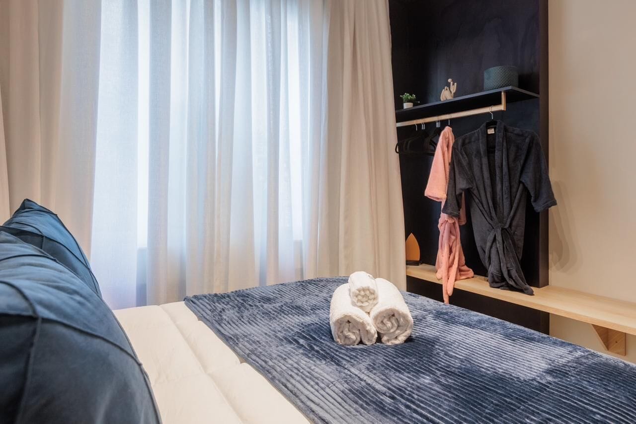 Ett hotellrum med en säng, ett sängbord, en garderob och ett fönster med gardiner.
