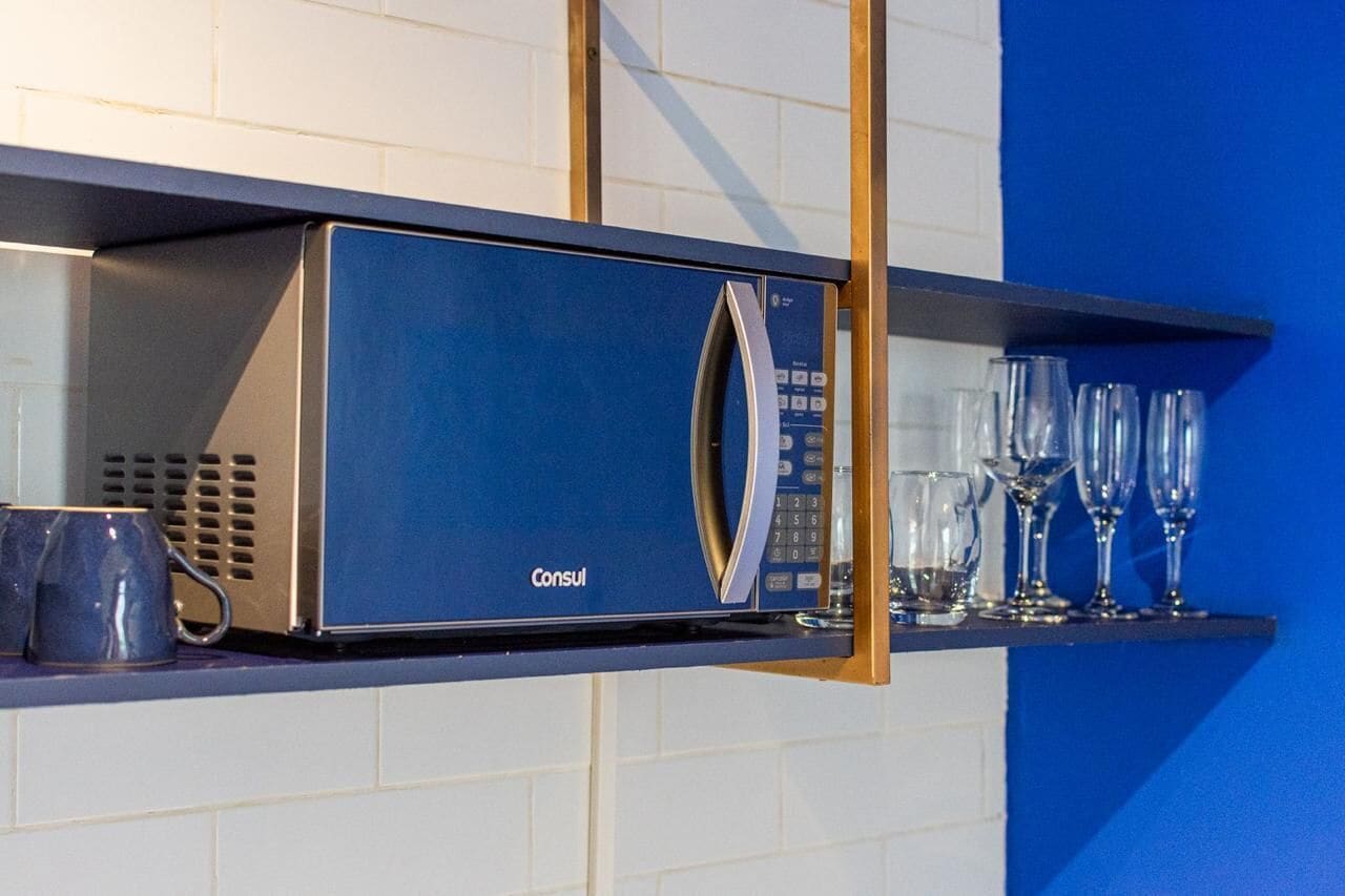 Eine blaue Mikrowelle mit digitaler Bedieneinheit, auf einer Ablage über einer gefliesten Wand platziert.