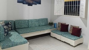 Una sala de estar con techo de madera, un ventanal con barrotes, un conjunto de sofás y una obra de arte colgada en la pared.