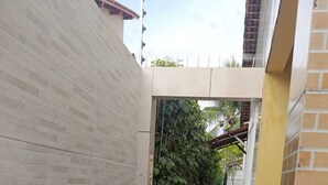 Un sendero estrecho bordeado por una pared de ladrillo blanco y otra de ladrillo amarillo, que conduce a una zona cubierta con techo metálico.