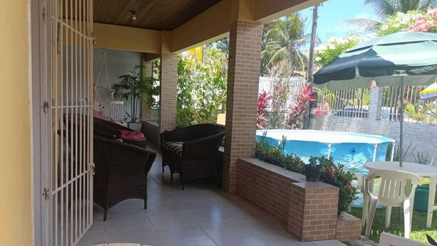 Un patio techado con muebles de mimbre, una piscina y vistas de vegetación tropical.