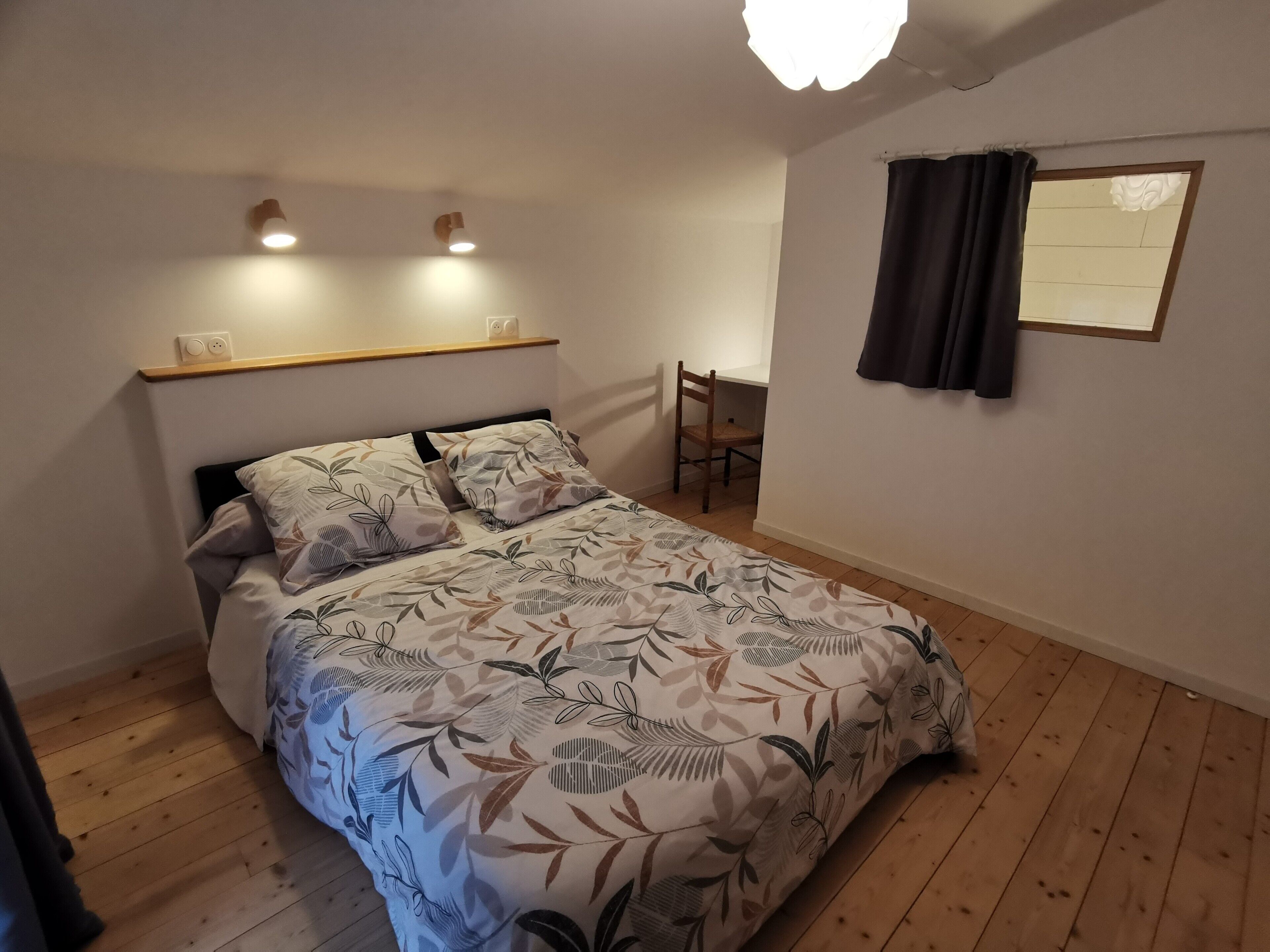A bedroom with a bed, a chair, a shelf with two light fixtures, and a window with a curtain.