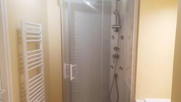 A glass-enclosed shower stall with a handheld showerhead and a handheld shower attachment.