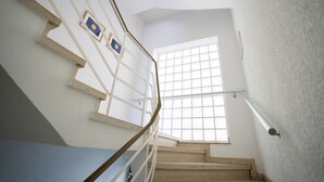 A staircase with a metal railing, a window with a grid pattern, and a wall-mounted light fixture. - Gästehaus Elena (Kassel)