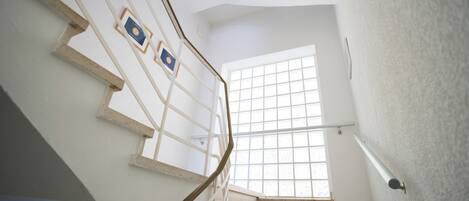Un escalier avec une rampe en métal, une fenêtre à croisillons et un luminaire fixé au mur.
