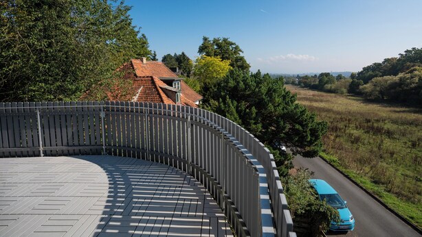 A curved wooden deck with a view of a road and trees. - Gästehaus Elena (Kassel)