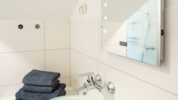 A bathroom with a glass sink, a mirror with lights, and a stack of towels.