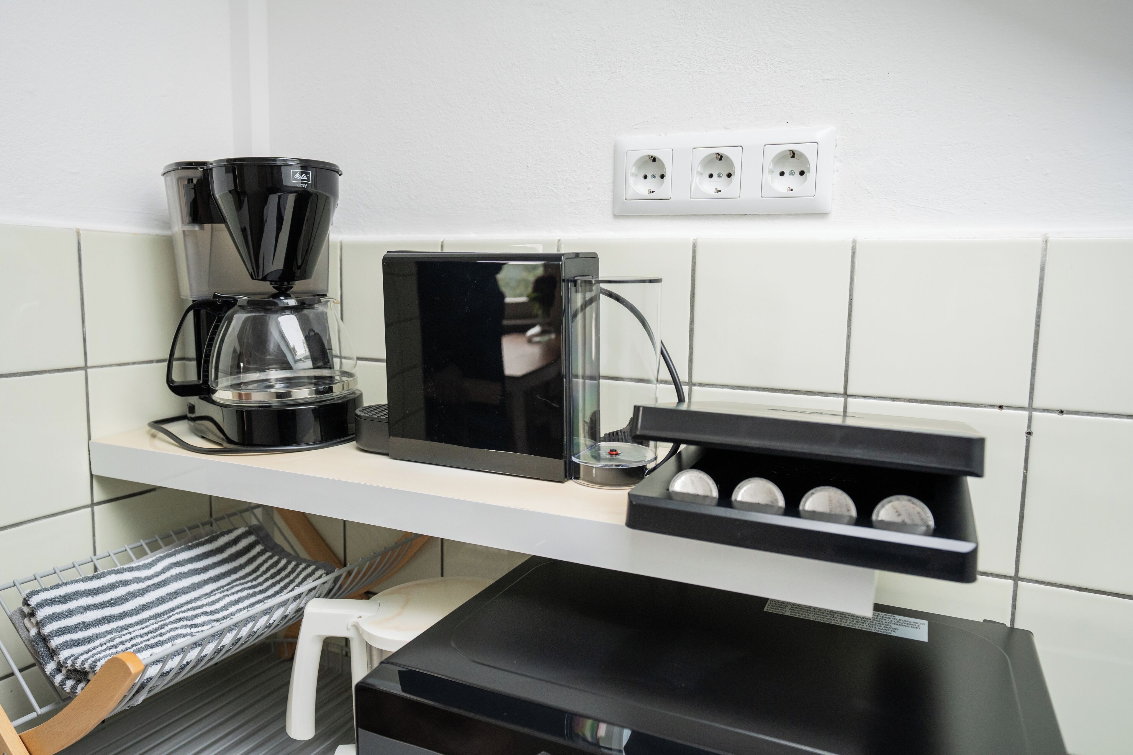 Une cuisine équipée d’une machine à café, d’un four à micro-ondes et d’une étagère avec trois verres.