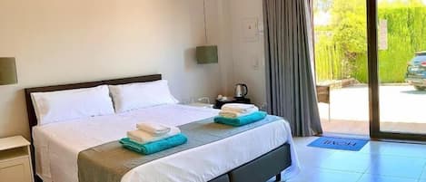 Une chambre à coucher avec un lit, des tables de chevet, une fenêtre avec des rideaux et une vue sur la verdure à l’extérieur.