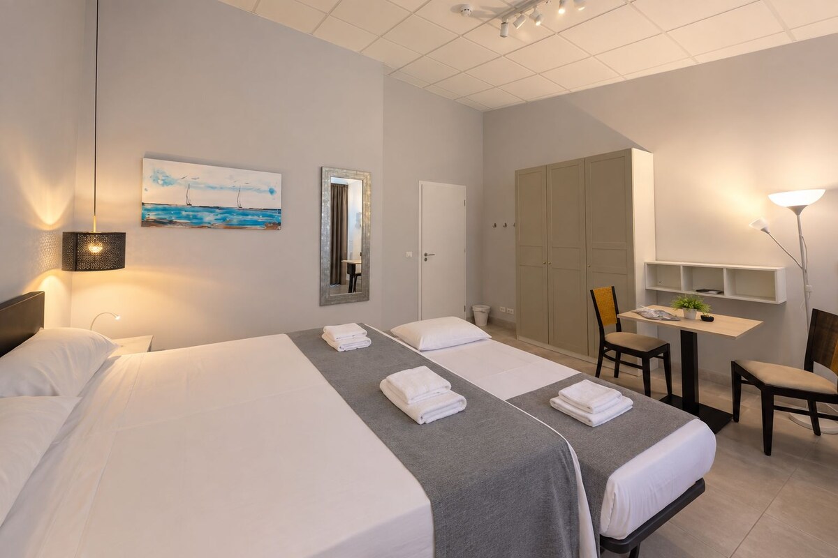 A hotel room with a large bed, a desk, a chair, a mirror, and a painting on the wall.