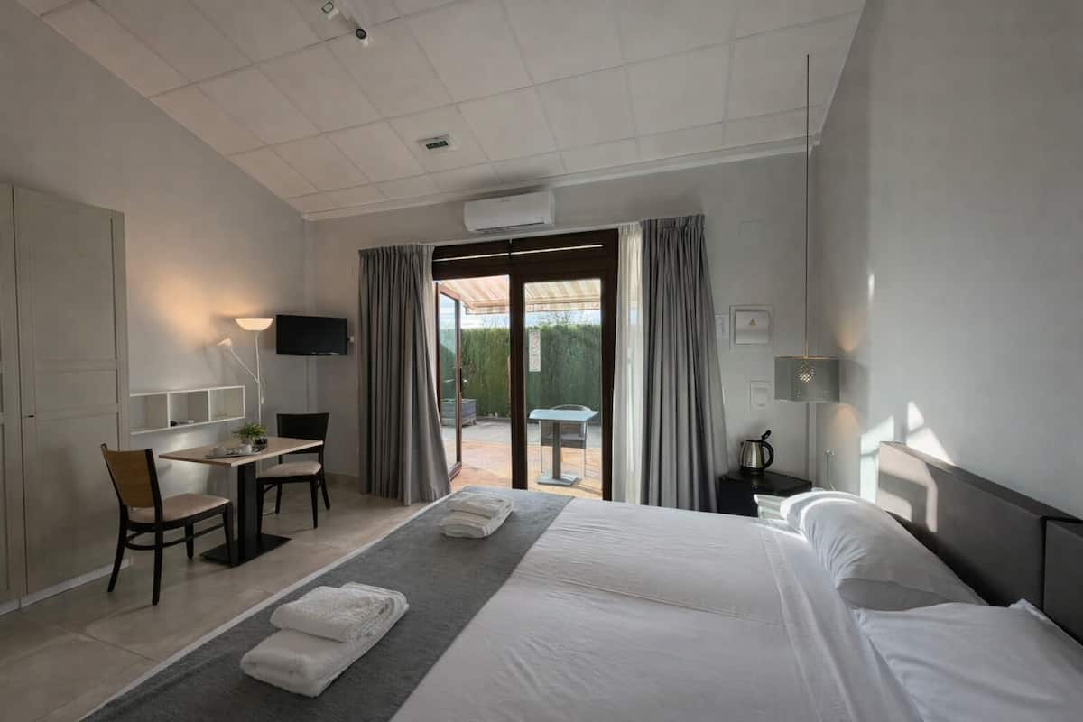 A hotel room with a bed, a desk, a chair, a TV, and a balcony with curtains.