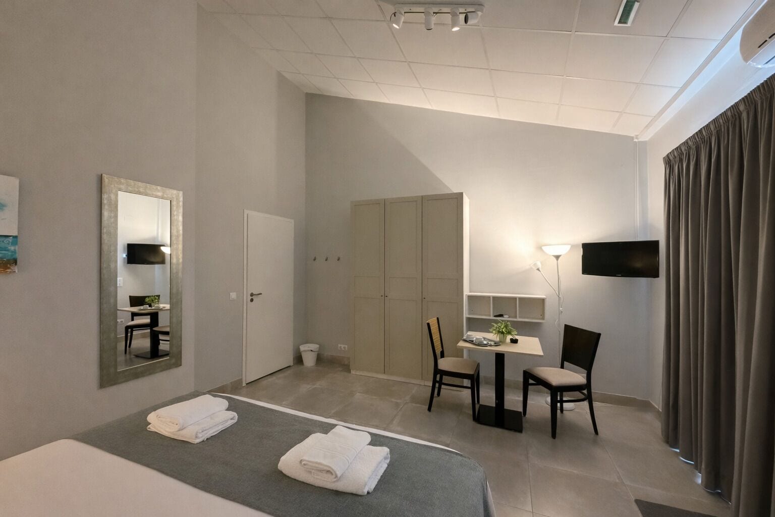 Una habitación de hotel con cama, escritorio, silla, televisor y armario.
