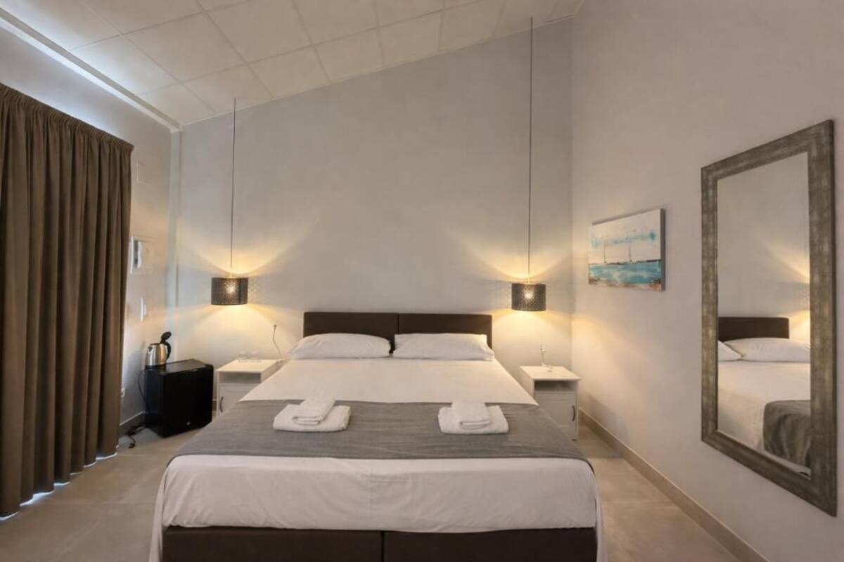 A hotel room with a large bed, two bedside tables, a nightstand, a lamp, a painting, and a mirror.