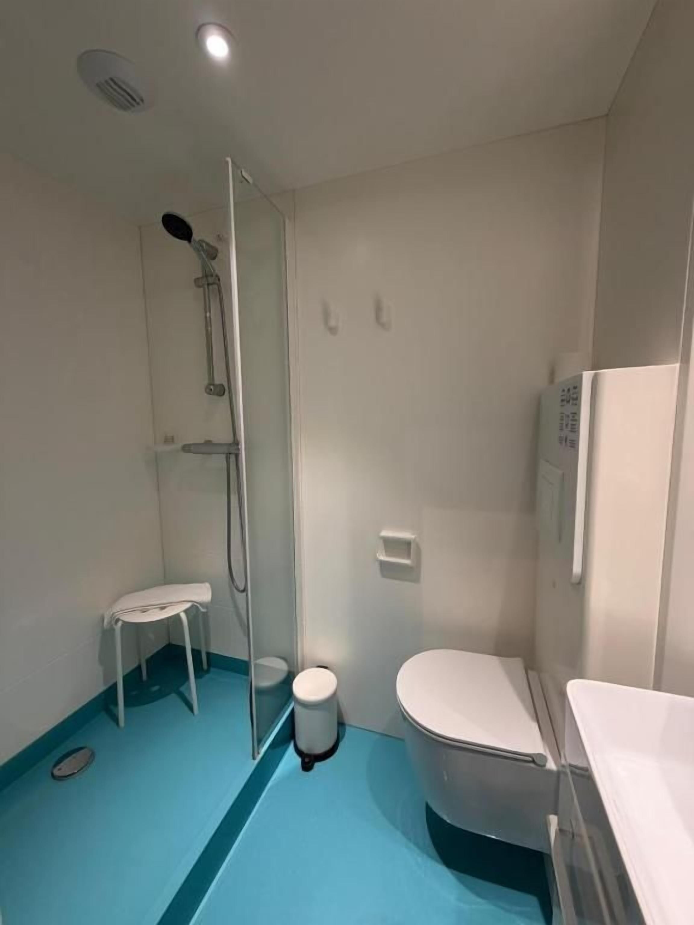 Kylpyhuone, jossa on suihku, wc ja pieni jakkara.