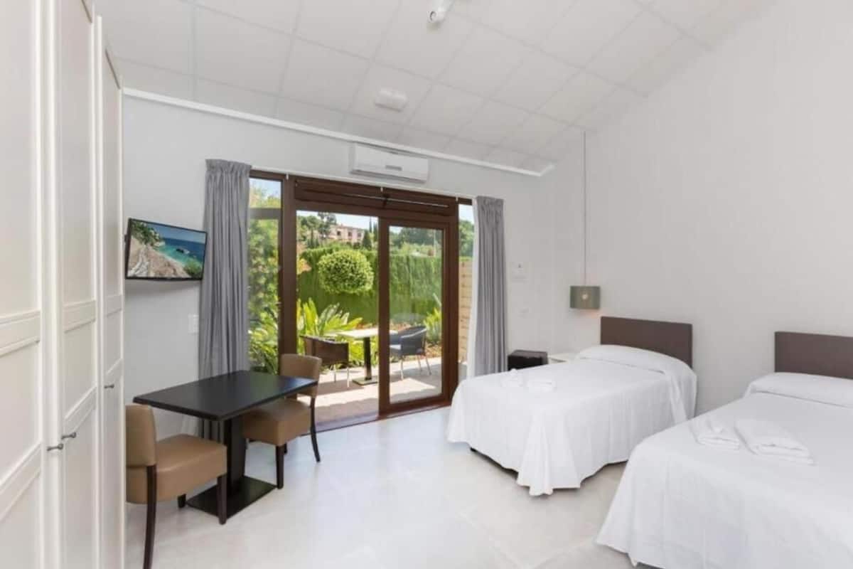 A hotel room with two beds, a desk, and a view of the outdoors.